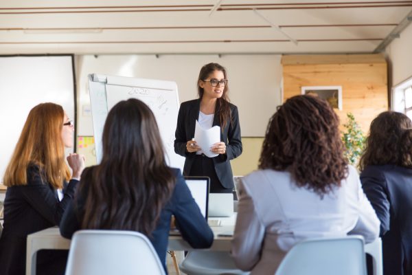 Businesswomen looking at speaker with papers. Group of professional multiethnic businesswomen looking at leader during meeting in office. Women in business concept