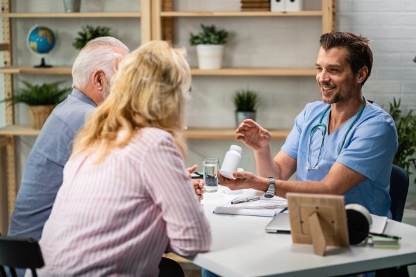 Happy doctor holding pill bottle while talking with senior couple about the vitamins they should be taking.